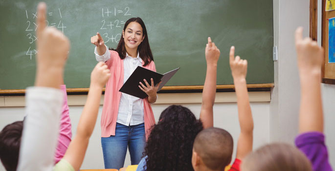 Teacher in front of classroom with children raising hands