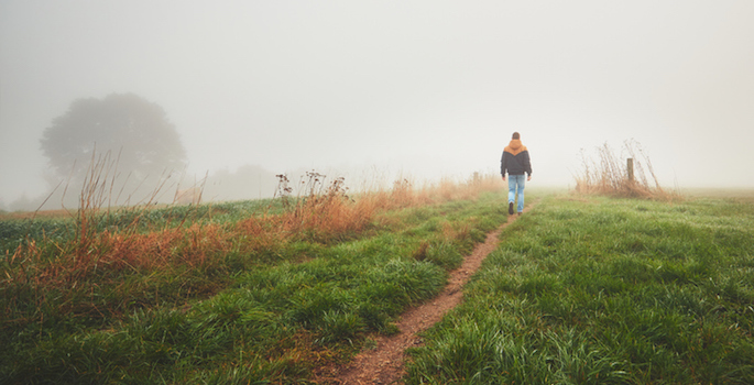 Lonely young white man walking on a path through a field on a foggy day