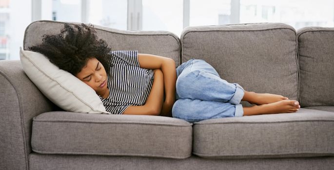 Shot of a young african american woman experiencing stomach pain on the sofa at home