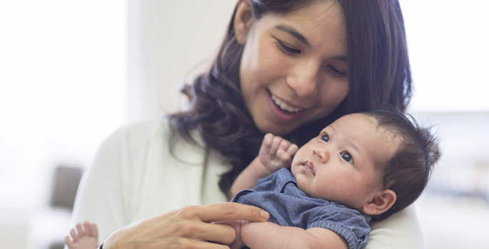 New mother smiling and holding newborn baby at home