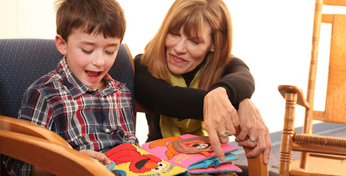 a middle aged woman instructs a young boy to read