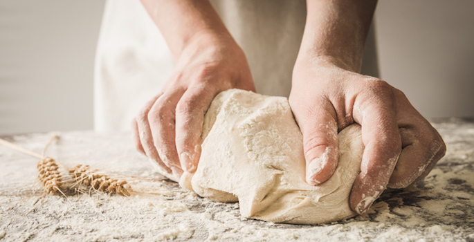 close up of hands kneading dough on floury surface