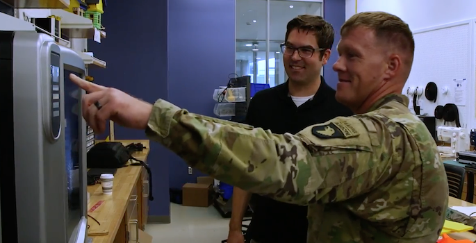 army guy pressing a button on a 3D printer while kevin galloway looks on