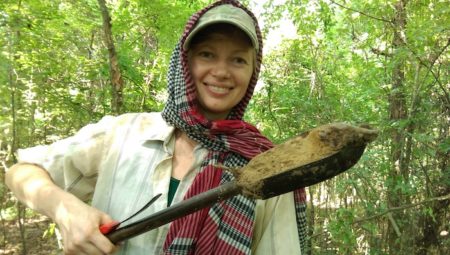 Liz posing with a shovel in the woods surrounding the mound