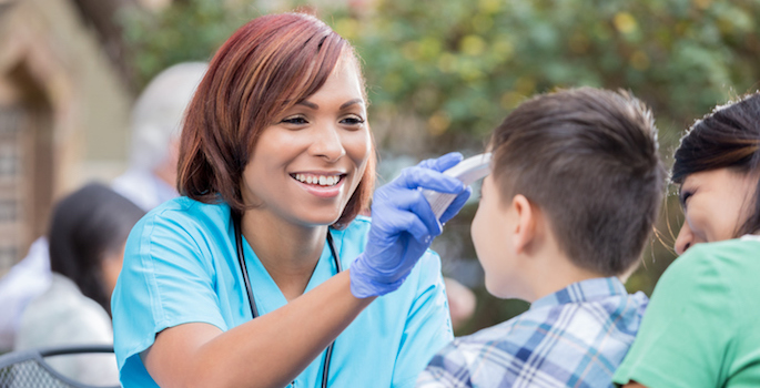 hispanic or african american nurse at outdoor clinic taking young boy's temperature