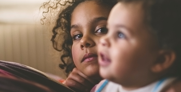 two biracial little girls appear to be watching a tv just out of frame