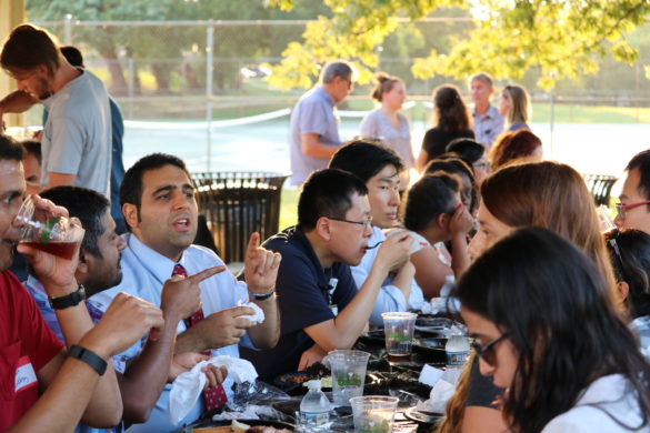 Postdocs and some children enjoying picnic meals at a long picnic table in the park