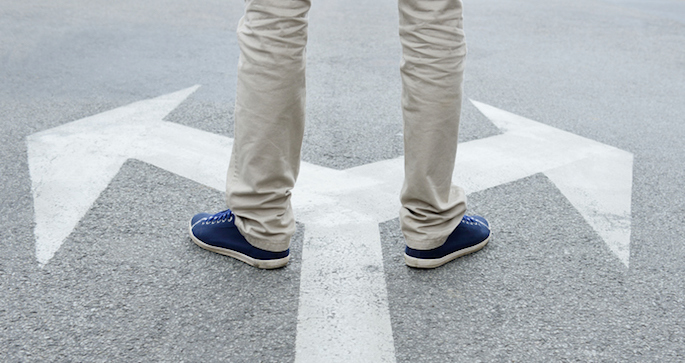 Decision concept - Man standing on arrows painted on asphalt.