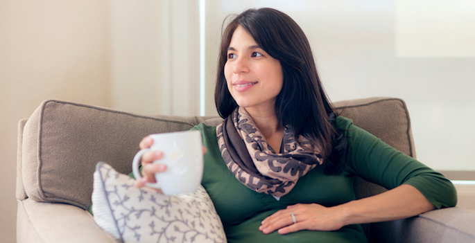 Adult pregnant woman sipping tea while looking out the window