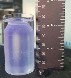 purplish crystal in a jar next to a ruler