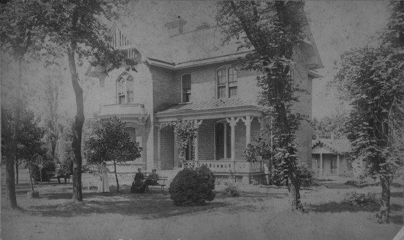 Black and white old fashioned photo of house and cottage with residents standing in yard