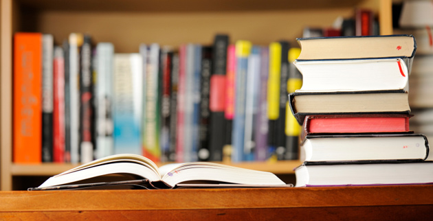 Open book and books piled up on a bookshelf