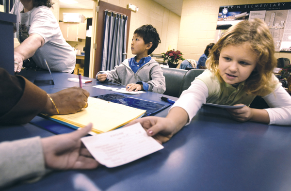 Grace Todd, right, hands a tardy slip to a student while Winston Zuo-yu, center, fills out more tardy slips at Eakin Elementary School. Eakin uses the Positive Behavior System developed by Peabody faculty member and researcher Kathleen Lane. After receiving tickets for positive behavior at school, children qualify to be chosen for responsible positions and other prizes. Zuo-yu and Todd were chosen to help in the school office as morning tardy officers.