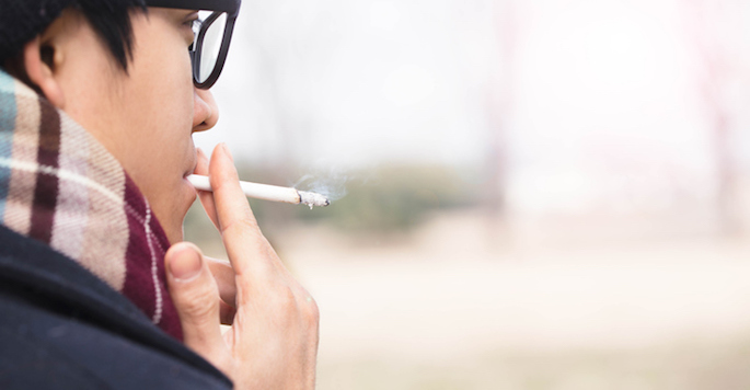 Profile of Asian man in glasses smoking a cigarette