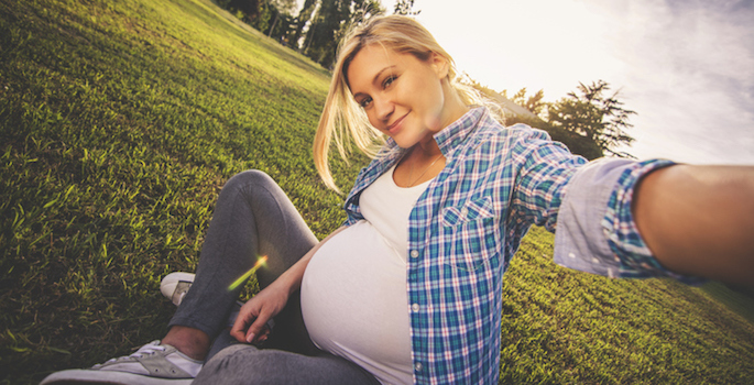 Young blond pregnant woman taking selfie outdoors