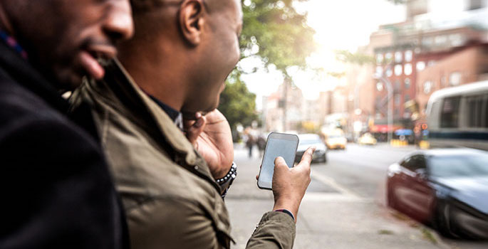 Two young African American men walking together on city street holding a smartphone