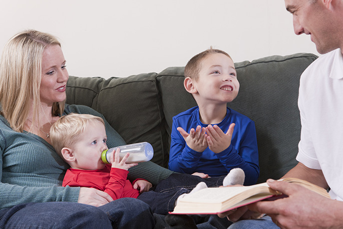 Boy signing the word 'Book' in American Sign Language while studying with his parents