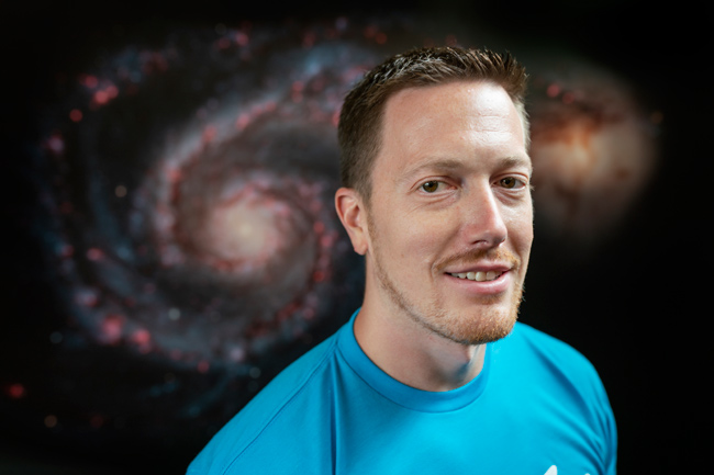 Billy Teets in front of an image of a nebula in space