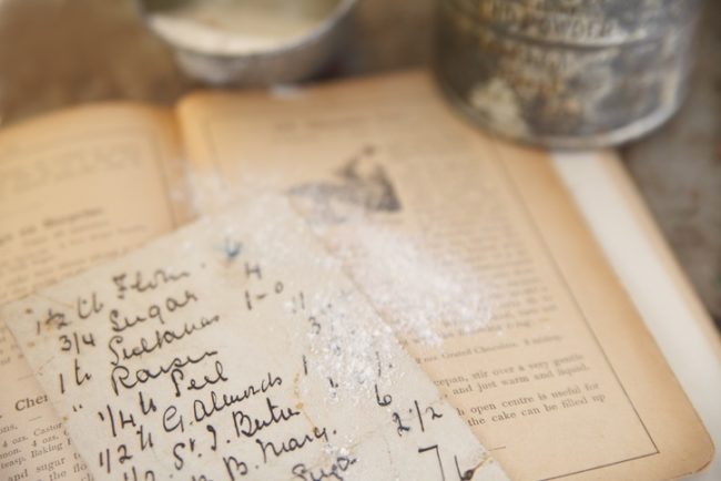 old recipe atop a cookbook from 1894 dusted with flour with vintage sifter and measuring cup in background (Getty)