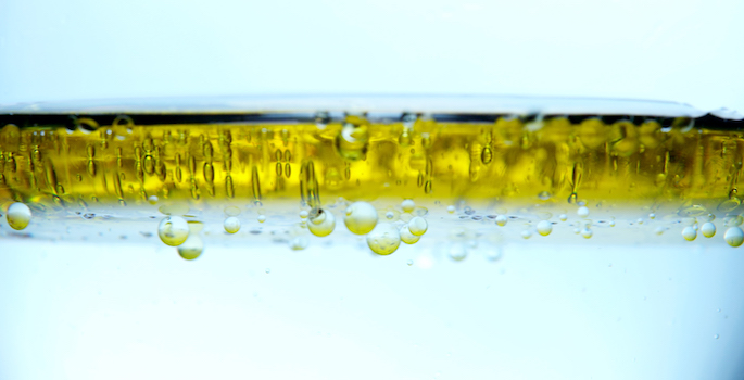 layer of olive oil on top of water with small bubbles of oil filtering down