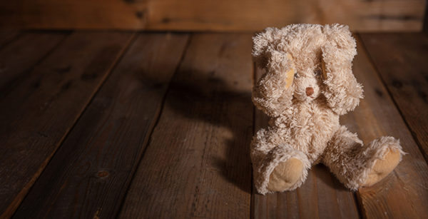 Child abuse concept. Teddy bear covering eyes, dark empty background, copy space