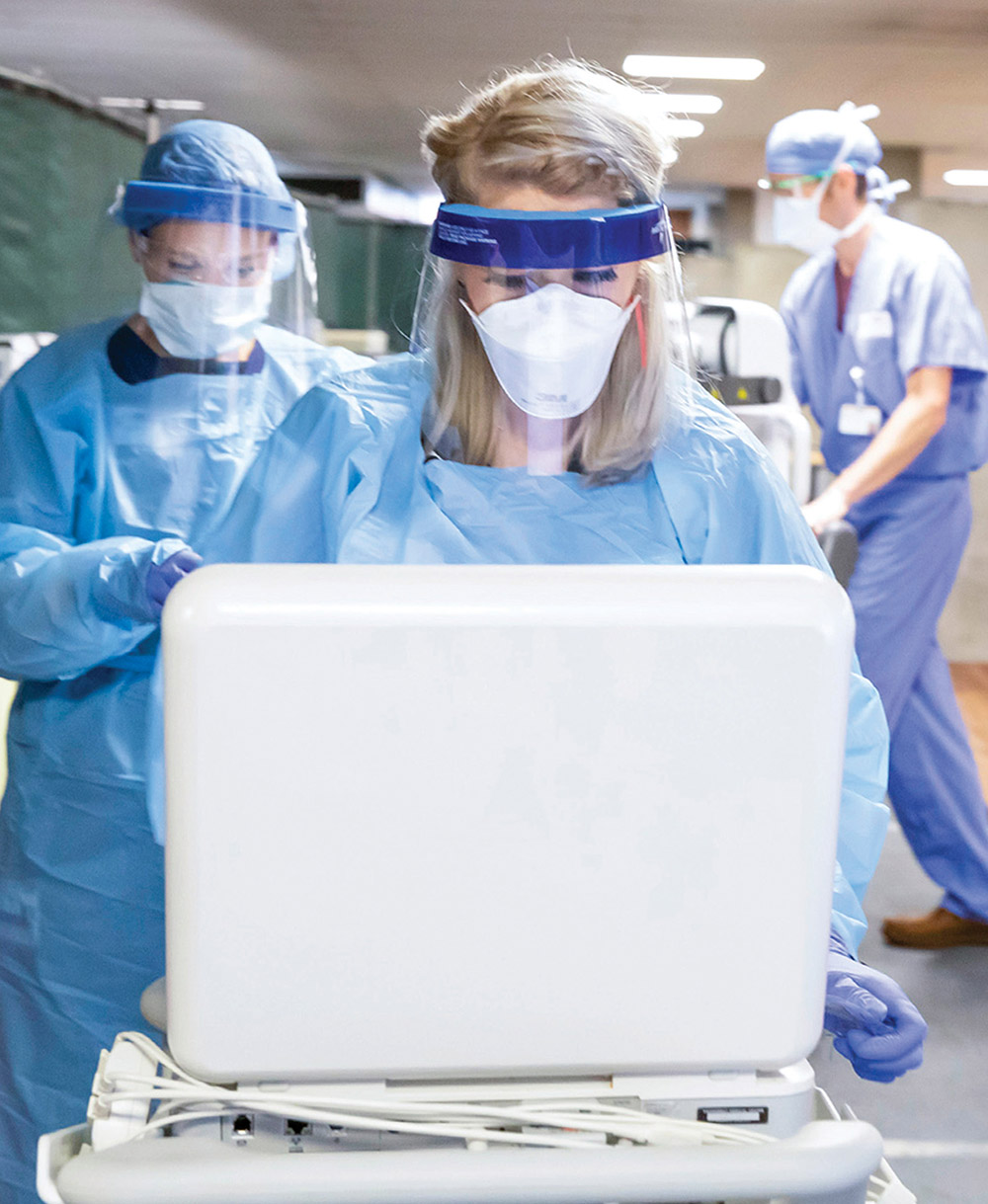 photo of health care workers in masks and scrubs looking at a laptop screen