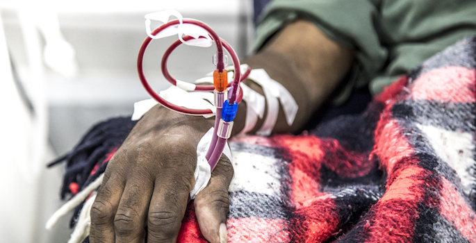Close-up of dialysis tubing taped to arm of elderly African American man, resting on a red plaid blanket