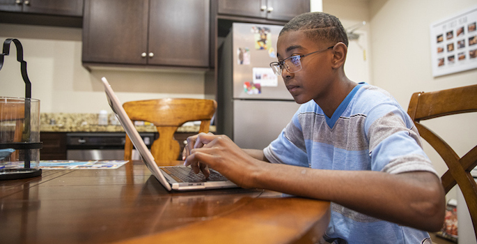 A young African American boy using a computer at his kitchen table