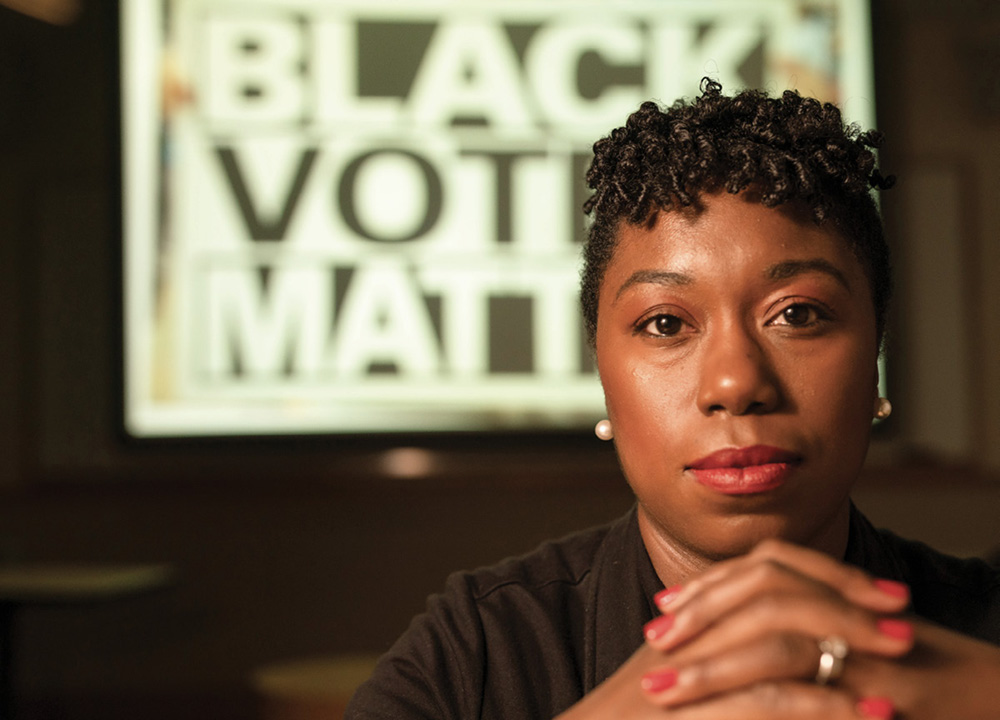 photo of Charlane Oliver in front of a sign that says "Black Votes Matter"