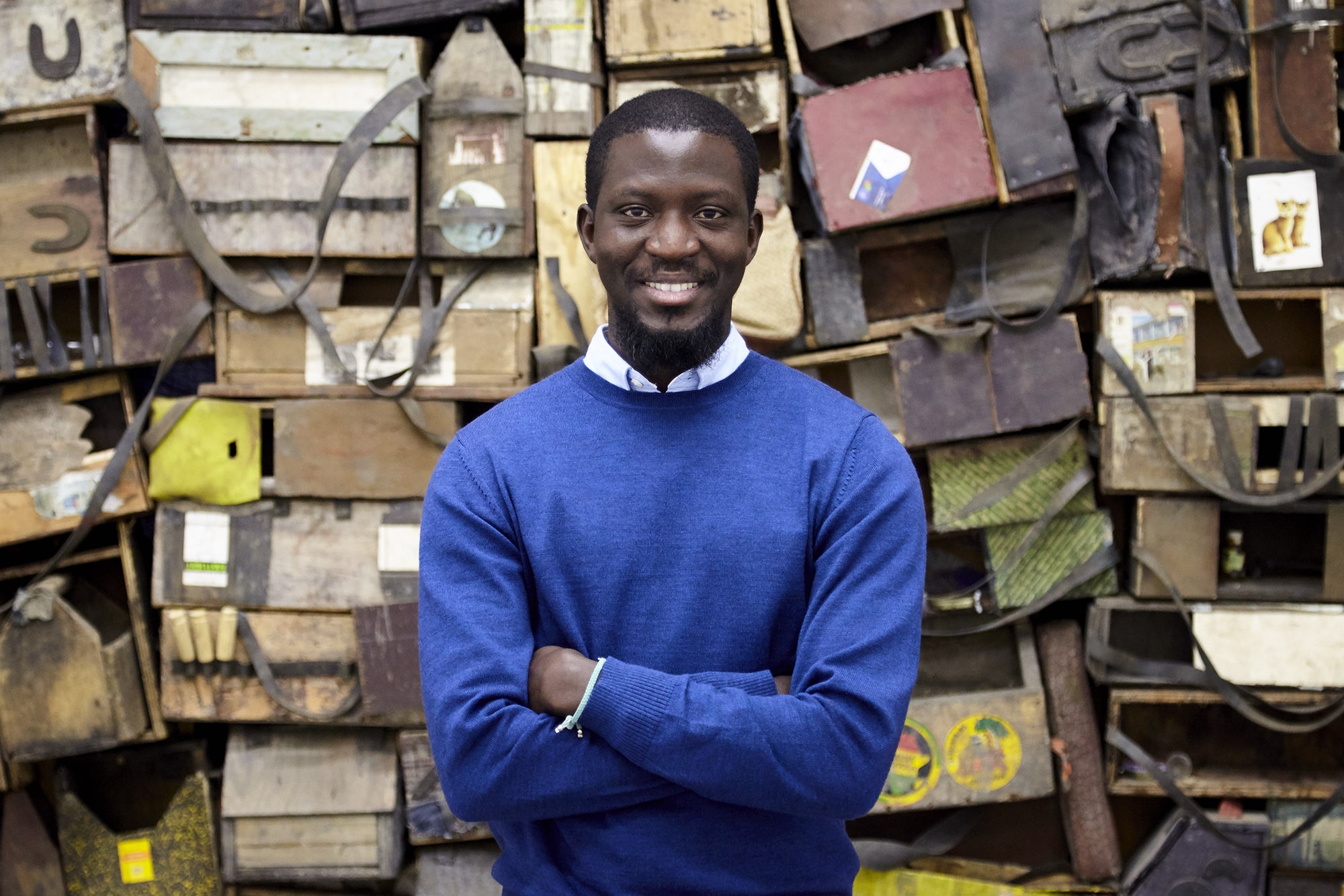 photograph of artist Ibrahim Mahama in front of jute sacks collected at Ghanian markets