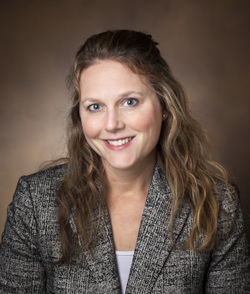 woman with light brown hair in gray blazer and white blouse