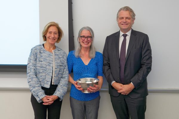 Provost C. Cybele Raver, Professor Meg Saylor, who is holding silver bowl, and Chancellor Daniel Diermeier standing in front of classroom white board 