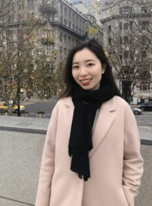 woman standing outside in a city wearing a pink coat and black neck scarf