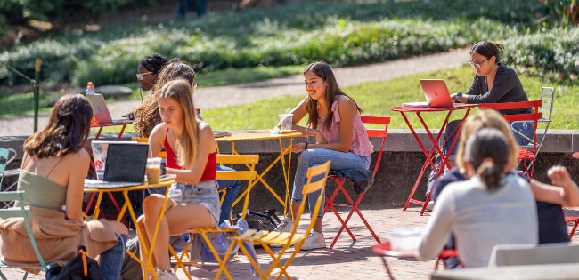 Students sitting at outdoor tables near Rand Hall.