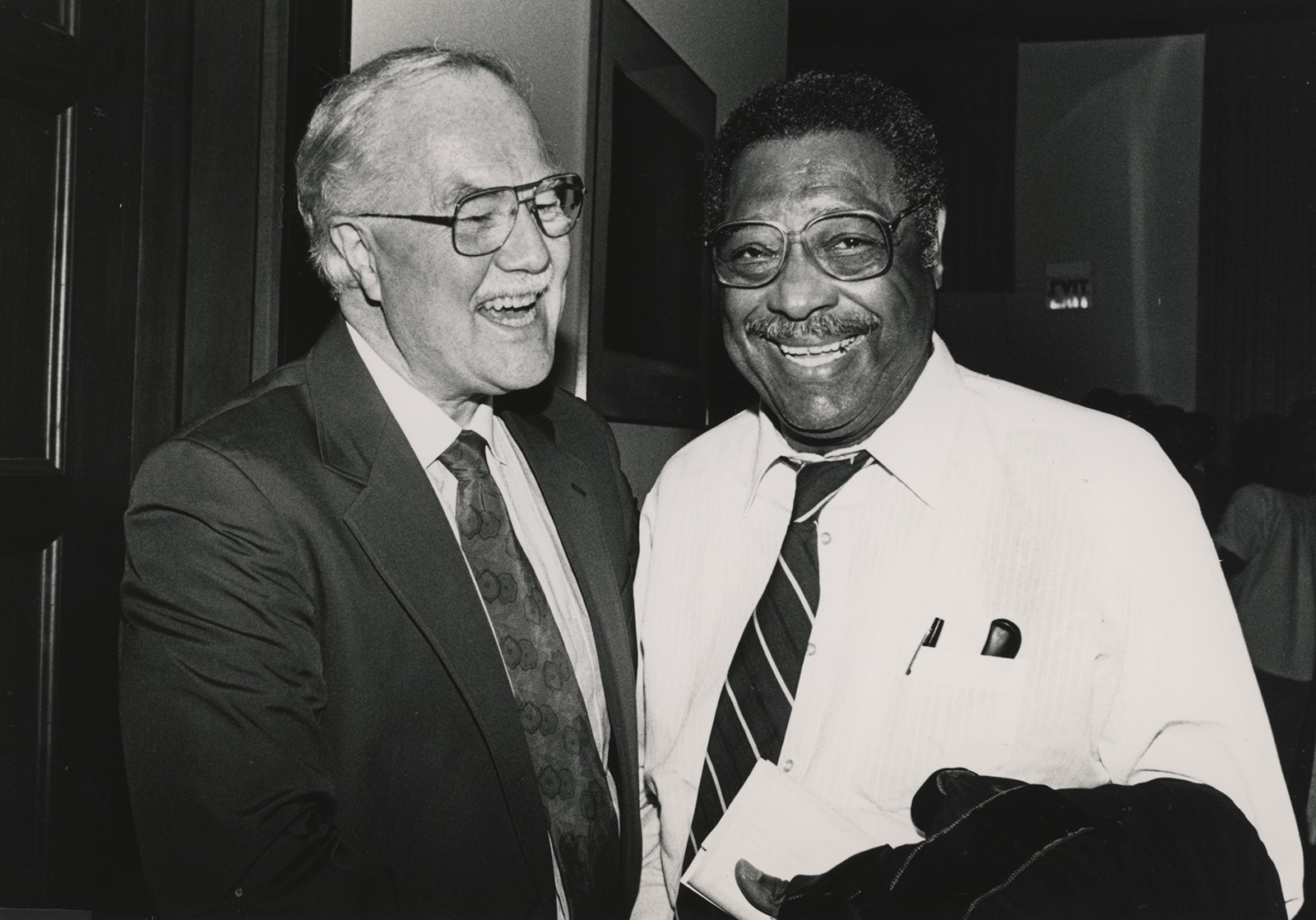 Two smiling men, one white, one Black, in a black and white photo taken at a reception