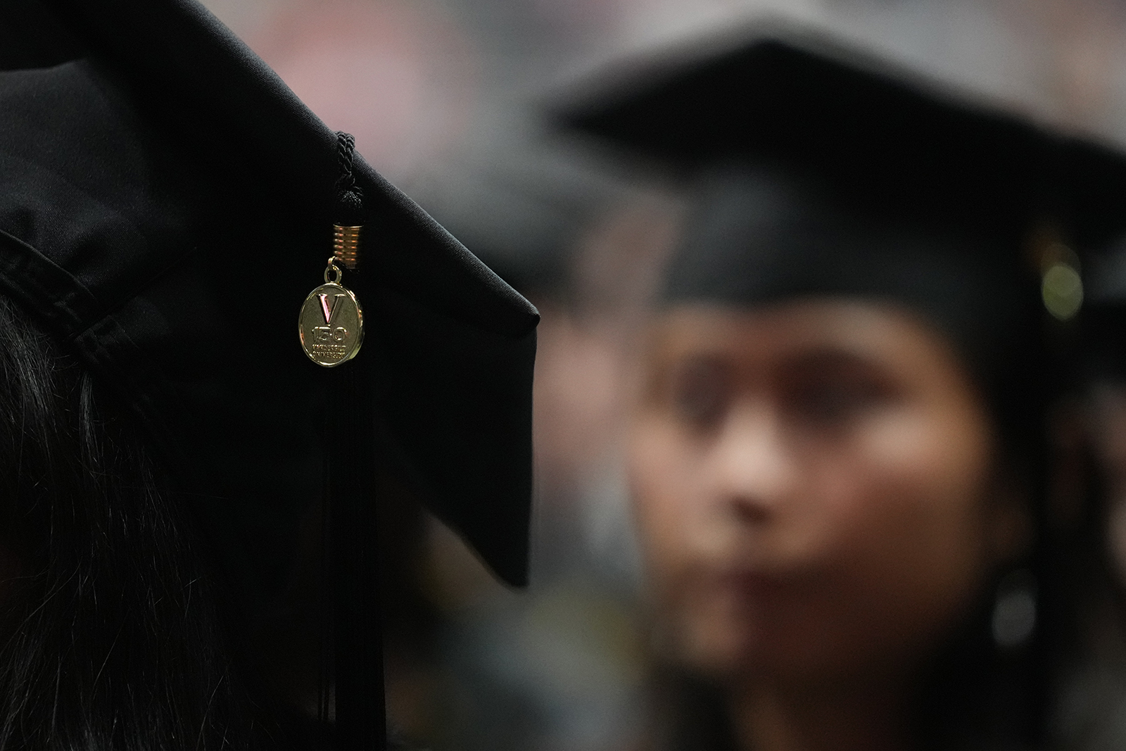 Vanderbilt University Commencement 05/12/23. Photo by Joe Howell. A close-up of the Vanderbilt Sesquicentennial charm on the tassel of a graduate's mortarboard with another graduate seen in hazy focus behind.