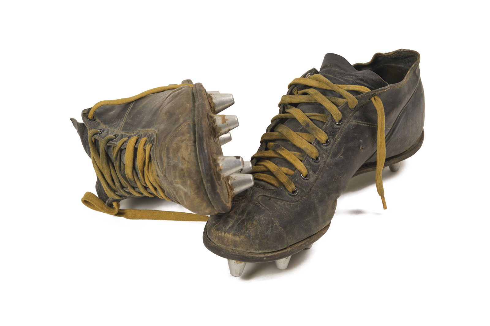 Dirty, cracked football cleats from the 1930s, with gold untied shoestrings, mud still on the bottom of the cleats