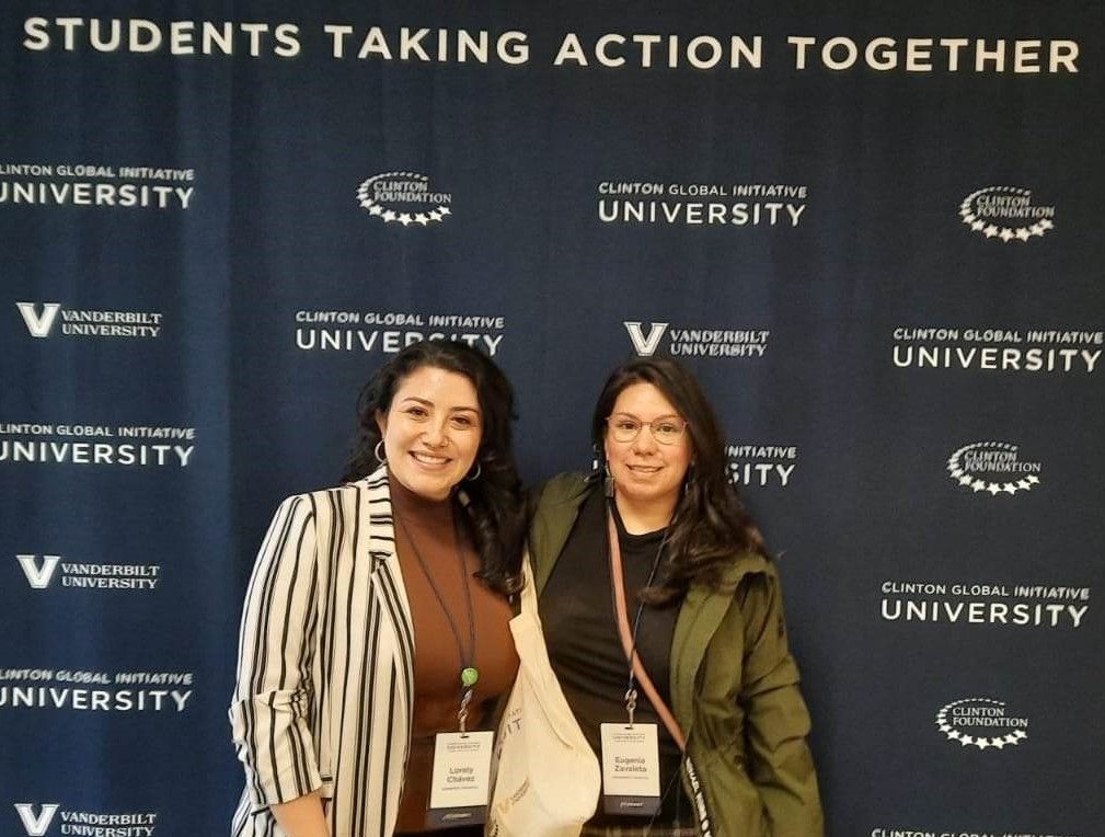 Two female students in front of banner for Clinton Global Initiative University