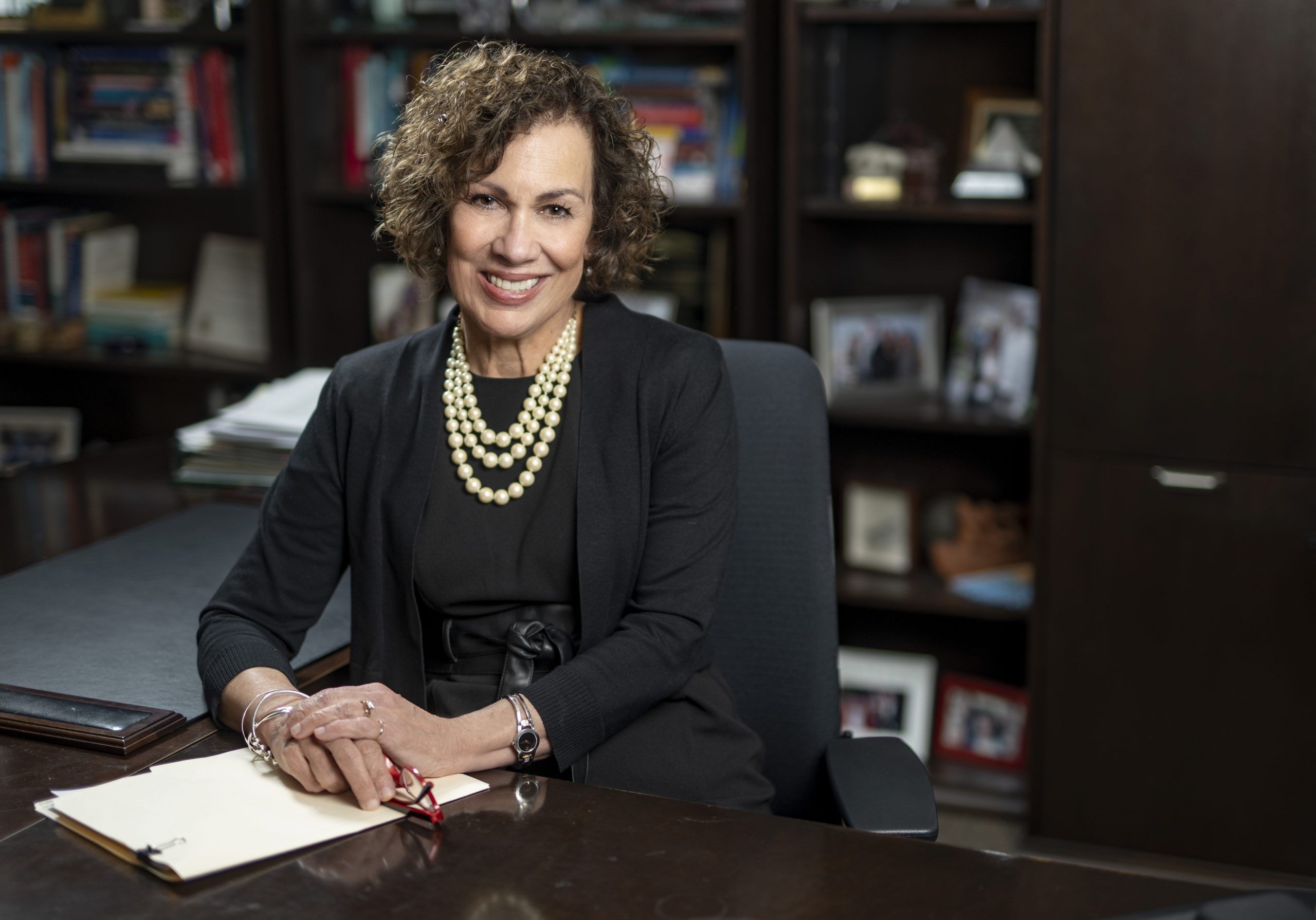 A woman sitting a desk with her hands folded over each other