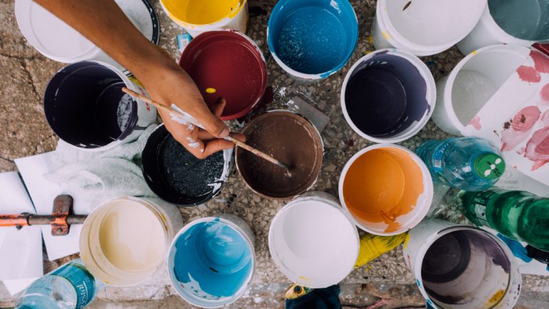 small containers of paint with a hand dipping a thin paintbrush into the brown paint container