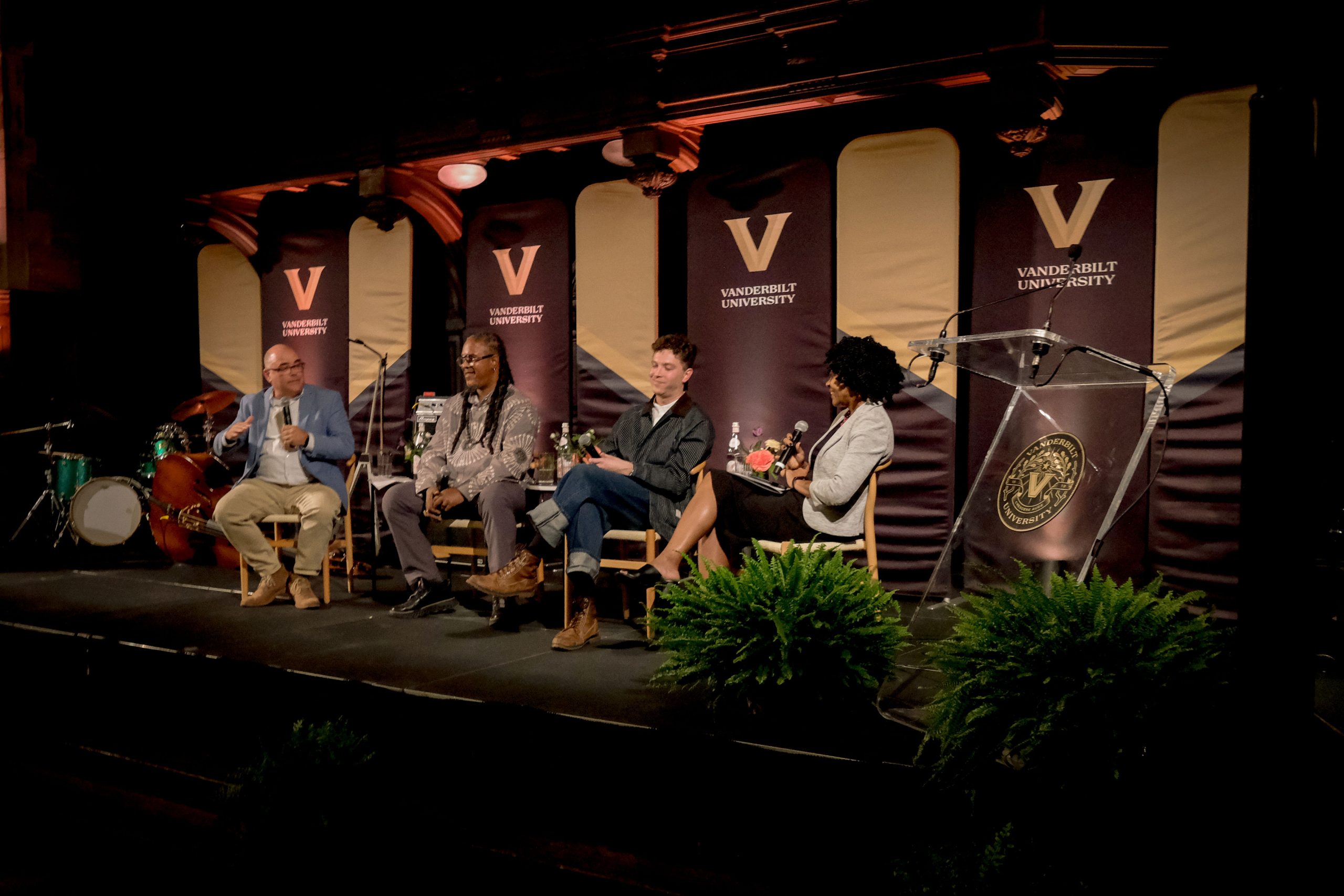 Panel speakers and moderators sit on a stage talking into microphones