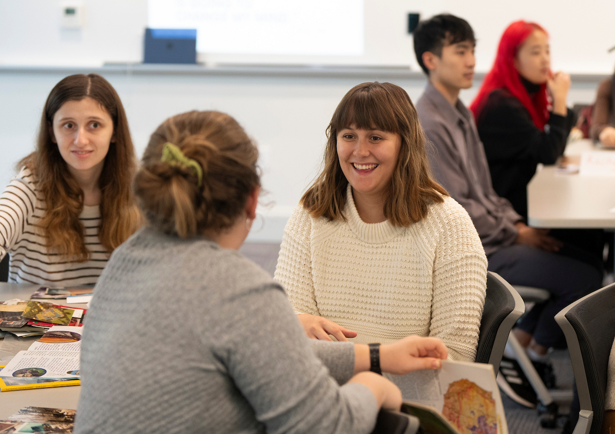 Two college students smiling and laughing in a classroom and sitting at a desk together