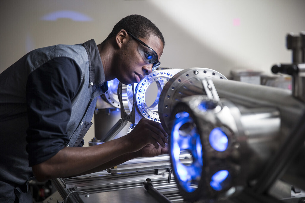 Researcher wearing safety glasses examines illuminated scientific equipment in a laboratory.