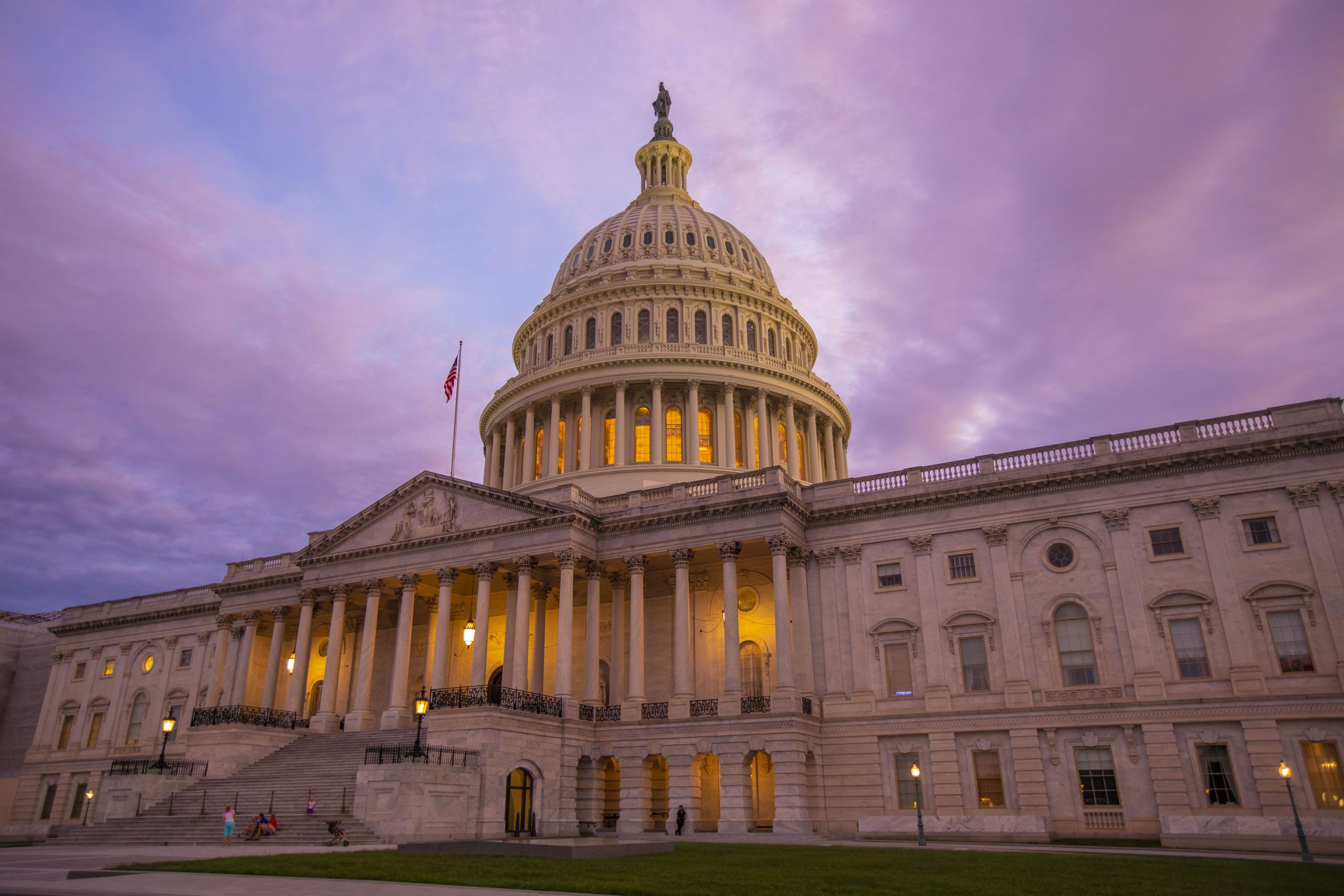 U.S. Capitol Building at dusk with lights glowing inside and a purple sky overhead.