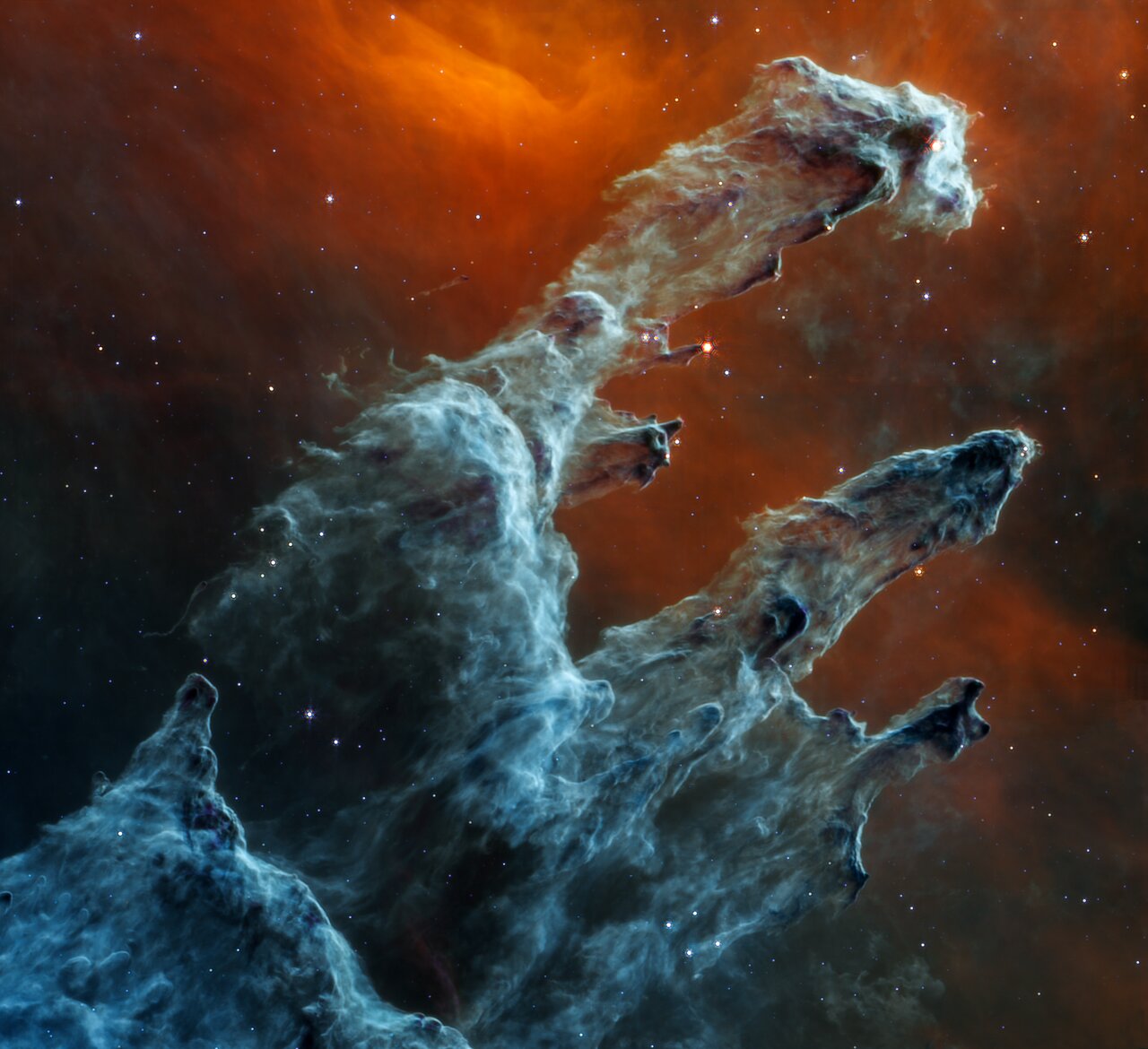 The Eagle Nebula's Pillars of Creation as seen in mid-infrared light with the James Webb Space Telescope. Stars appear much fainter and less numerous in longer (redder) wavelengths of light however, warm (orange) and cool (blue and grey) dust glow brightly. At the ends of the pillars a few embedded stars can be seen glowing as bright reddish-orange points as they heat up the gas and dust surrounding them. Credit: NASA, ESA, CSA, STScI; Image Processing: Joseph DePasquale (STScI), Alyssa Pagan (STScI)