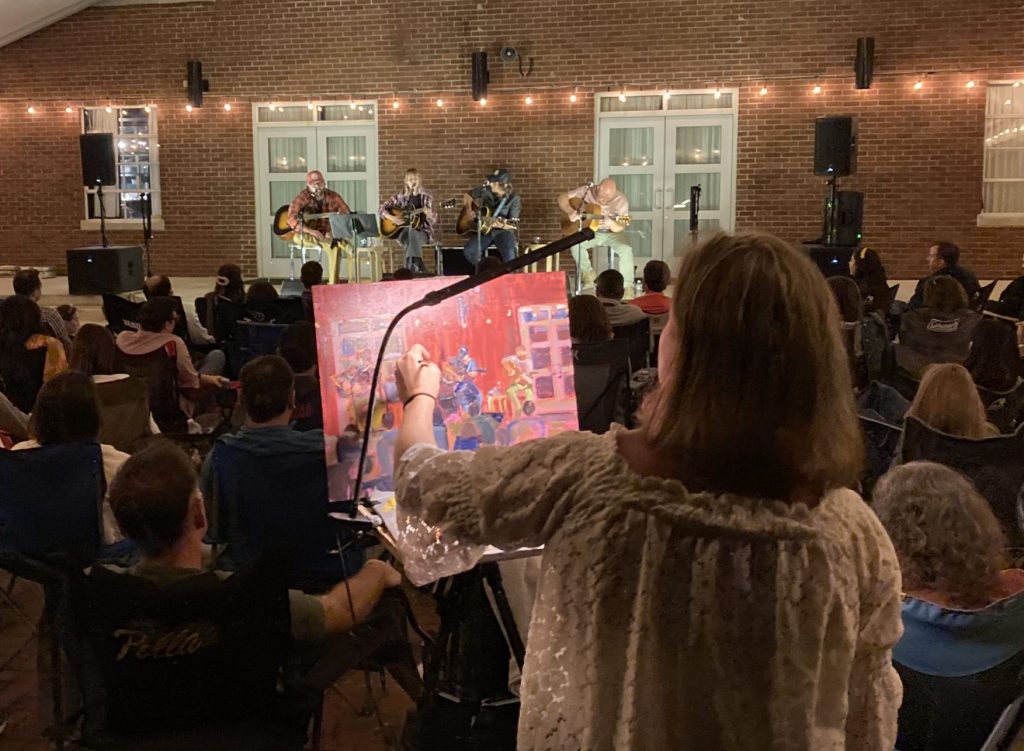 Crowd under the Dyer tent with songwriters on the stage and an illustrative painting beind done in the foreground