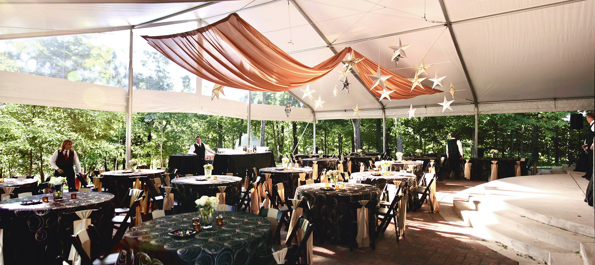 Outdoor event space at Vanderbilt Dyer Observatory with a large tent, round tables, hanging star decorations, and forest backdrop, set for a formal gathering.