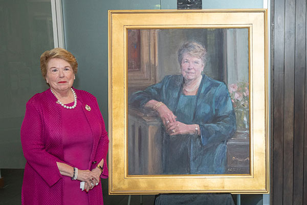 Dean Linda Norman stands next to an oil portrait of herself 