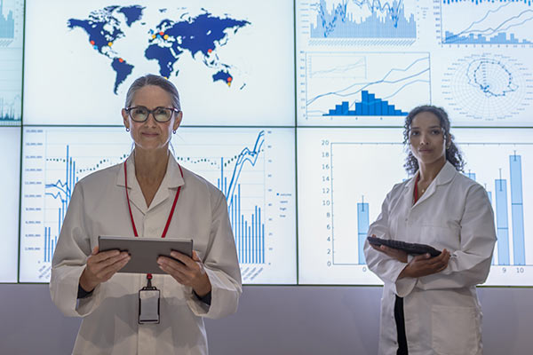 Nurse informaticists with tablets stand in front of digital screens with graph and data