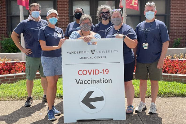 A group of Vanderbilt volunteers wear face masks and pose with a sign that says VUSN/VUMC COVID-19 Vaccination with an arrow pointing to the vaccination site